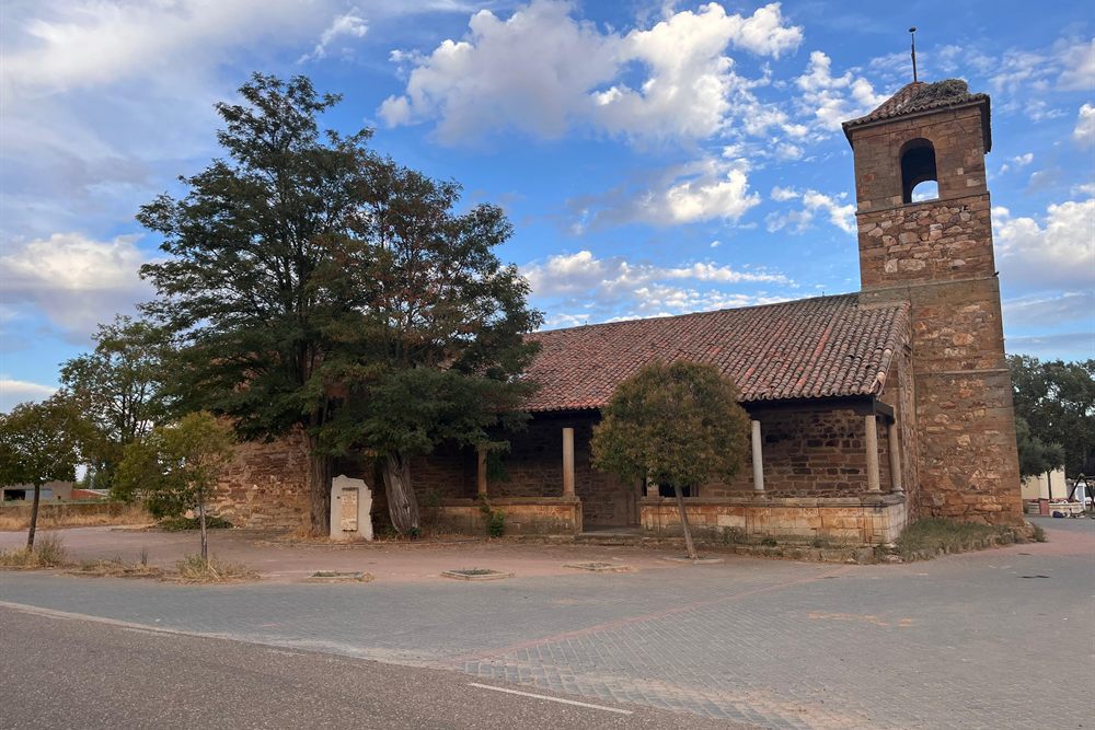 La iglesia de San Miguel Arcángel desde la carretera, con el pórtico de columnas y la torre coronada por un nido de cigüeña.