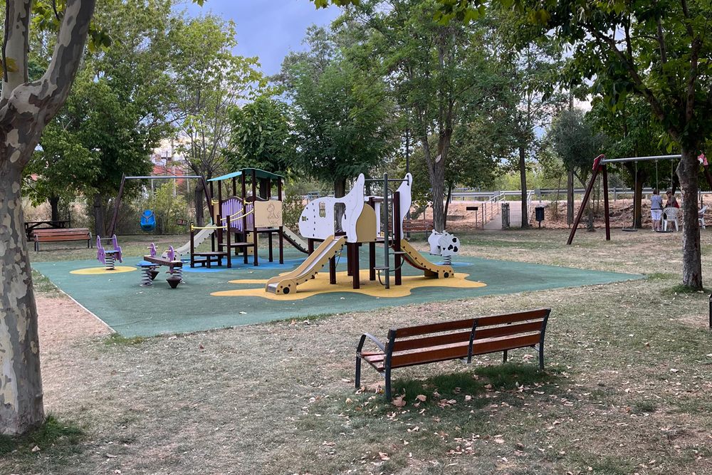 Parque infantil del pueblo, con juegos y columpios bajo los plátanos.