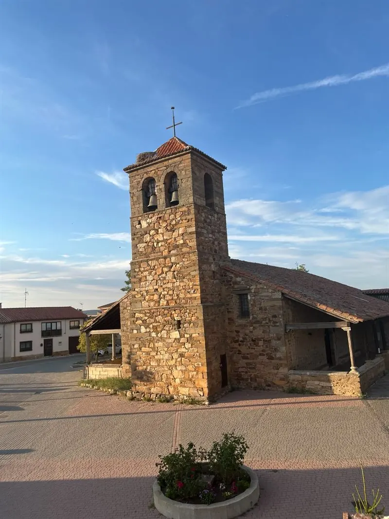 Iglesia de San Miguel Arcángel al atardecer, con su torre de piedra, la espadaña con dos campanas y un nido de cigüeña